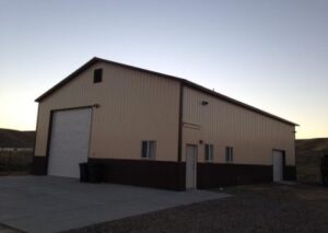 A large, metal-clad storage building with a roll-up door and two side windows, set against a dusky sky and gravel ground
