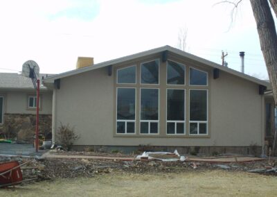 A tan home addition with a gable roof and a large central window wall composed of six rectangular glass panes