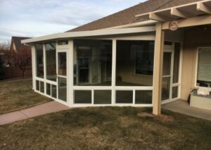 A large white-framed glass sunroom addition on the back of a tan house, featuring multiple glass panels and a side entry door